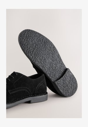 Schwarzer Veloursleder-Schnürschuh mit strukturiertem Gummisohlen, versehen mit gesteppten Akzenten und abgerundetem Zehendesign.