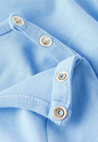 Jasnoniebieska tkanina o widocznej strukturze; posiada srebrne zatrzaski wzdłuż krawędzi, starannie przyszyte, co wskazuje na staranność w projektowaniu odzieży.