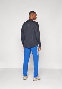 Long-sleeve shirt in dark gray, with black accents, paired with blue pants featuring a side pocket and textured patches.