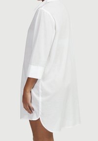 Weißes Hemdblusenkleid aus Leinen mit lockerem Schnitt, ausgestattet mit Kragen, halben Ärmeln und abgerundetem Saum. Seitenschlitze sorgen für zusätzlichen Komfort und Bewegungsfreiheit.