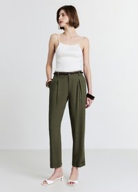 Débardeur blanc côtelé et pantalon taille haute vert olive avec plis, accessoirisé d'une ceinture marron et de talons ouverts blancs.