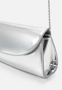 Hopeinen metallinen clutch-laukku, jossa on taitettava läppä, ketjuhihna ja ommellut reunat. Liukas pinta, jossa on kiiltävä heijastava pinta.