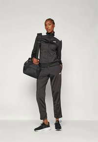 Melnas sporta treniņtērps, izgatavots no gludas auduma, ar ar rāvējslēdzēju aizveramu virsjakas un pieguļošām biksēm. Akcentēts ar baltu logotipa detaļu un savienots ar melnu somu.