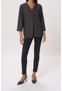 Černá texturovaná halenka s výstřihem do V a tříčtvrtečními rukávy, kombinovaná s úzkými černými kalhotami a černými lodičkami se špičatou špičkou.