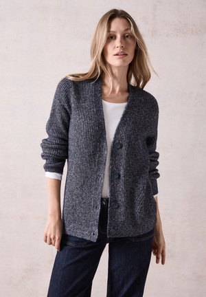 Knitted cardigan in dark grey with a textured pattern, five buttons, and a shawl collar. Paired with a white top and dark jeans.