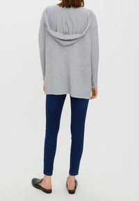 Šedá mikina s kapucí, volného střihu, texturovaná látka a detail zadního švu, v kombinaci s tmavě modrými skinny džíny a černými nazouvacími botami.