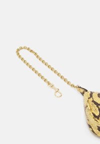 Łańcuszek z metalowymi złotymi ogniwami i zapięciem, przymocowany do torebki o wężowym wzorze w kolorze żółtym i czarnym, z fakturowaną powierzchnią.