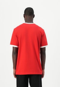 Κόκκινο κοντομάνικο μπλουζάκι με στρογγυλή λαιμόκοψη, με λευκά ένθετα στα μανίκια και στο λαιμό. Φτιαγμένο από μαλακό, ελαφρύ ύφασμα.