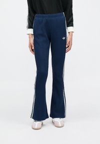 Tengerészkék bordázott, szárában bővülő nadrág fehér oldalsávokkal és kis hímzett logóval. Rugalmas derékrész a kényelemért.