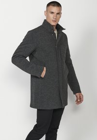 Abrigo de mezcla de lana gris con un cuello alto, diseño de corte recto, bolsillos laterales y un cierre delantero limpio. Acentuado con detalles de costura.
