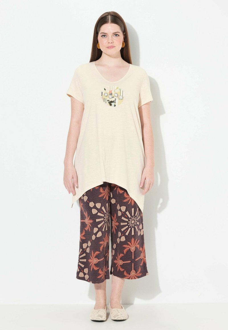 Crème t-shirt met een ronde halslijn en een bloemenmotief op de zak, gecombineerd met gestreepte, wijde broekspijpen in donkerbruin en oranje tinten.