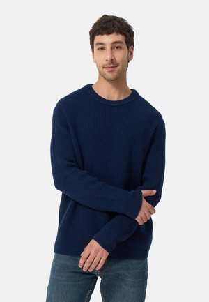 Granatowy sweter z dzianiny o prążkowanej strukturze, okrągłym dekolcie i długich rękawach, zestawiony z niebieskimi dżinsami. Luźny krój i wygodny design.