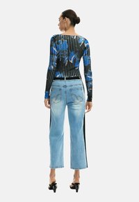 Pikad varrukadega pluus musta ja sinise lillemustriga, kombineeritud helepesuga teksadega, millel on must küljeriba ja lõdvestunud lõige.