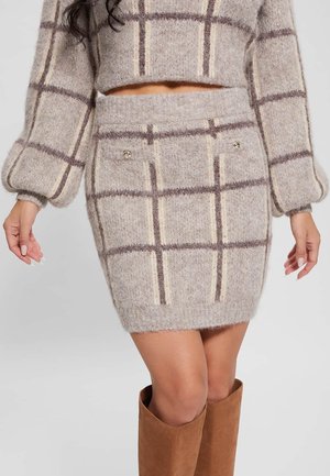 Kvinde iført beige og brun ternet fuzzy strikket nederdel og matchende langærmet cropped sweater med brune knælange støvler.