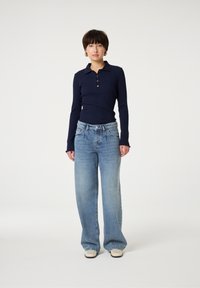 Marineblauwe ribbel polo met lange mouwen en drie knopen, gecombineerd met lichtblauwe wijdlopende jeans met een verwoeste zoom en een relaxte pasvorm.