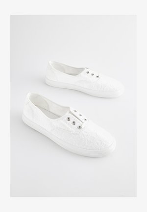 Białe koronkowe tenisówki z fakturowanym kwiatowym wzorem, elastycznymi bokami i srebrnymi przelotkami na sznurówki. Gumowe podeszwy zapewniają przyczepność.