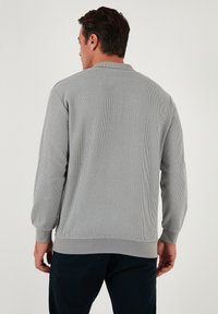 Tricou lung cu mânecă dintr-un material ribat de culoare gri deschis, cu guler rotund, având un tiv de jos și manșete ajustate. Țesătură texturată și croială adaptată.