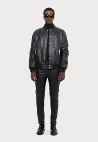 Black leather bomber jacket with snap buttons, ribbed cuffs, and waistband, paired with slim-fit black leather pants and black shoes.