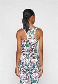 Kvinne med mørkt hår i hestehale som bærer en multicolor abstrakt trykt racerback tanktop og matchende leggings, stående med ryggen til kameraet.