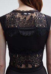 Czarna sukienka z misternym czarnym koronkowym wykończeniem na plecach, z florystycznymi wzorami i frędzlami, kontrastującymi z jednolitym materiałem podstawowym.