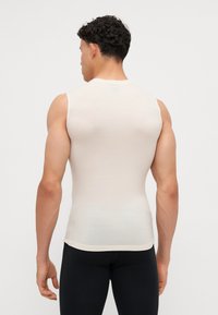 Chemise sans manches ajustée beige, fabriquée à partir d'un matériau léger avec une texture lisse. Encolure ronde, design uni et détail de couture aux épaules.