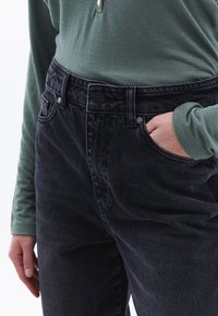 Jeans de mezclilla azul oscuro con cintura alta, bolsillos frontales y un cierre de un solo botón. Combinados con una blusa de manga larga verde.