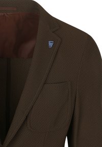 Brauner, strukturierten Blazer mit schmalem Revers, einer einzelnen Brusttasche und blauen Logo-Details am Kragen. Glatte, braune Innenauskleidung ist sichtbar.