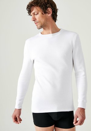 Camiseta ajustada de manga larga, blanca y hecha de tela suave, con un escote redondo y textura suave, combinada con unos calzoncillos negros.