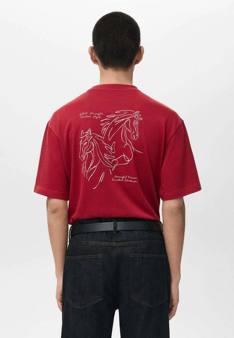 Tricou roșu din bumbac, cu desene lineare albe ale unui cal pe spate și text. Modelul poartă blugi închiși la culoare și o curea neagră.