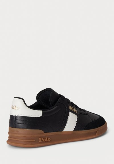 Zwart-witte sneaker met een gladleren bovenwerk, rubberen zool en gouden accenten. Inclusief vetersluiting en gevoerde kraag.
