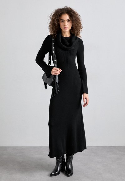 Ribbed black knit dress with a cowl neckline, long sleeves, and a fitted silhouette, paired with a black handbag featuring metal accents.