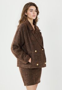 Braun gemusterte doppelt knöpfbare Jacke mit großen goldenen Knöpfen, kombiniert mit einem passenden Strickrock, ausgestattet mit einem lässigen Kragen und seitlichen Taschen.