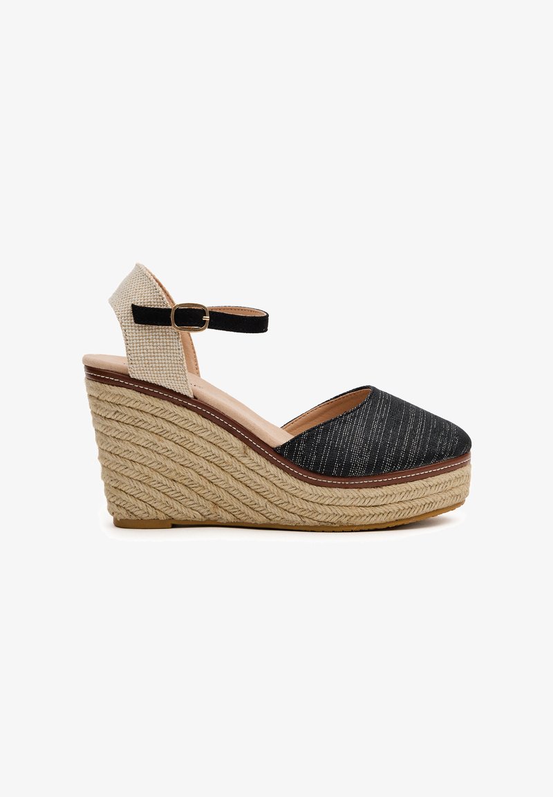 Sandalia cuña negra de lona con suela de yute trenzado, tira en el tobillo y soporte de tela texturizada beige. Presenta una puntera cerrada y un diseño minimalista.
