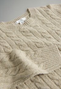 Beige knitted sweater with a textured cable pattern, ribbed neckline and hem, made of soft material, displayed on a light background.