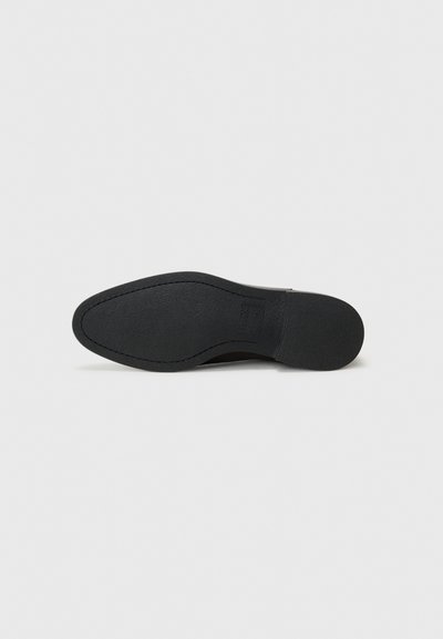 Suela de zapato negra con una superficie texturizada, forma ligeramente curvada y borde liso. Presenta un logotipo grabado en el lateral.