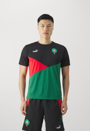 Camiseta atlética en negro, verde y rojo con mangas cortas, que presenta un patrón diagonal, el logo de Puma y un emblema marroquí. Se lleva con pantalones cortos negros.