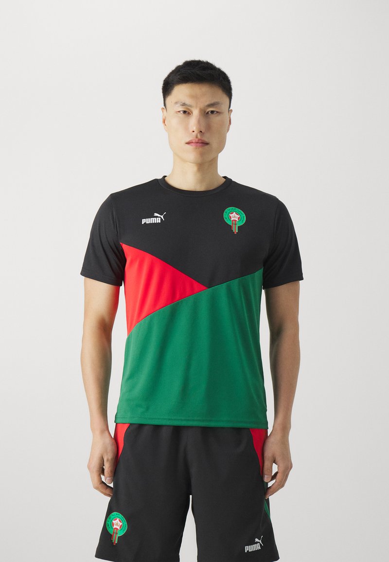 Camiseta atlética en negro, verde y rojo con mangas cortas, que presenta un patrón diagonal, el logo de Puma y un emblema marroquí. Se lleva con pantalones cortos negros.
