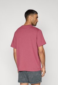 Κοντομάνικη μπλούζα με στρογγυλή λαιμόκοψη σε χρώμα σκονισμένο ροζ, κατασκευασμένη από απαλό ύφασμα, με άνετη εφαρμογή και επίπεδες ραφές. Φαίνεται από πίσω.