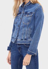 Blue denim jacket with a classic collar, two chest pockets, and button closures. Features a slightly faded texture and structured fit.