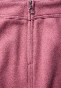 Rosa fleece-tyg med en slät textur, som har en vertikal söm och en metalldragkedja med ett runt draghandtag högst upp.