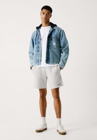Chaqueta de mezclilla con capucha, color azul claro, con un bolsillo frontal, llevada sobre una camiseta blanca y combinada con pantalones cortos grises y zapatillas blancas.
