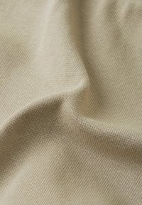 Beżowa, teksturowana tkanina o drobnym, dzianinowym wzorze. Powierzchnia jest gładka, prezentująca subtelne różnice w odcieniach i głębokości splotu.