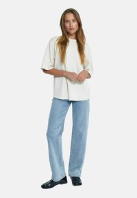 Camiseta de algodón crema de gran tamaño con escote redondo, combinada con unos vaqueros rectos de color azul claro y unos mocasines negros brillantes.