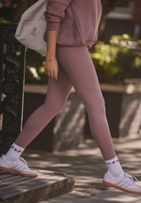 Heledad lilla retuusid siledast materjalist, koos valgete spordijalatsite ja mustriliste pahkluusokkidega. Riietus on juhusliku, hugate disainiga.