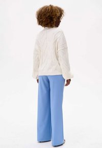 White cable-knit sweater with a high neck, paired with light blue wide-leg trousers. Textured knit pattern on the sweater adds detail.
