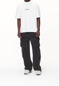 Bílé tričko s krátkým rukávem a černým potiskem, šedé cargo kalhoty s několika kapsami a volným střihem, doplněné o šedé tenisky.