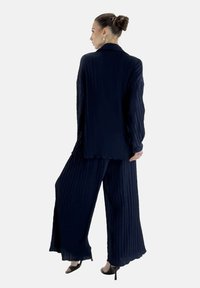 Conjunto de dos piezas en azul marino que incluye una blusa de manga larga con cuello y pantalones de pierna ancha con tejido texturizado y diseño plisado.