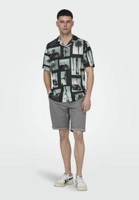 Camisa de manga corta y botones con un estampado fotográfico en blanco y negro, combinada con pantalones cortos grises y zapatillas blancas.