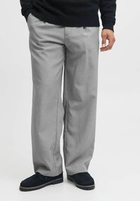 Pantaloni gri deschis, comozi, cu un design ajustat, av�ând pliseuri și buzunare laterale, asortați cu pantofi negri.
