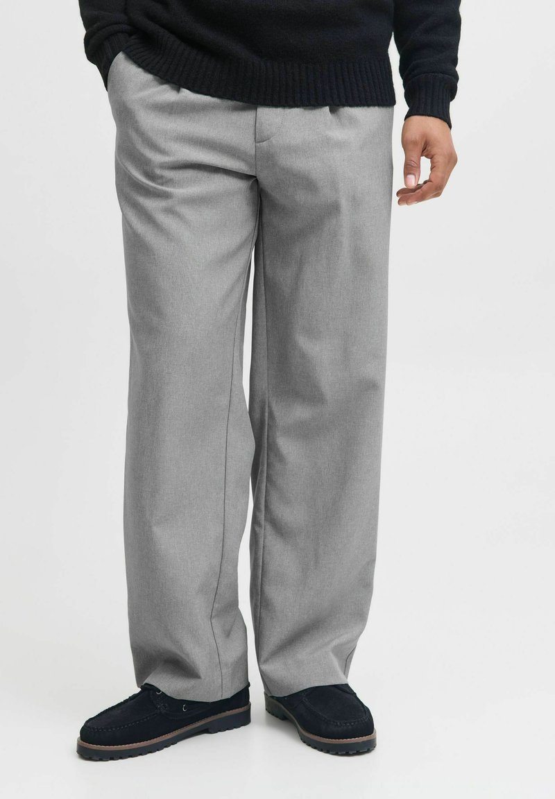 Pantaloni gri deschis, comozi, cu un design ajustat, având pliseuri și buzunare laterale, asortați cu pantofi negri.